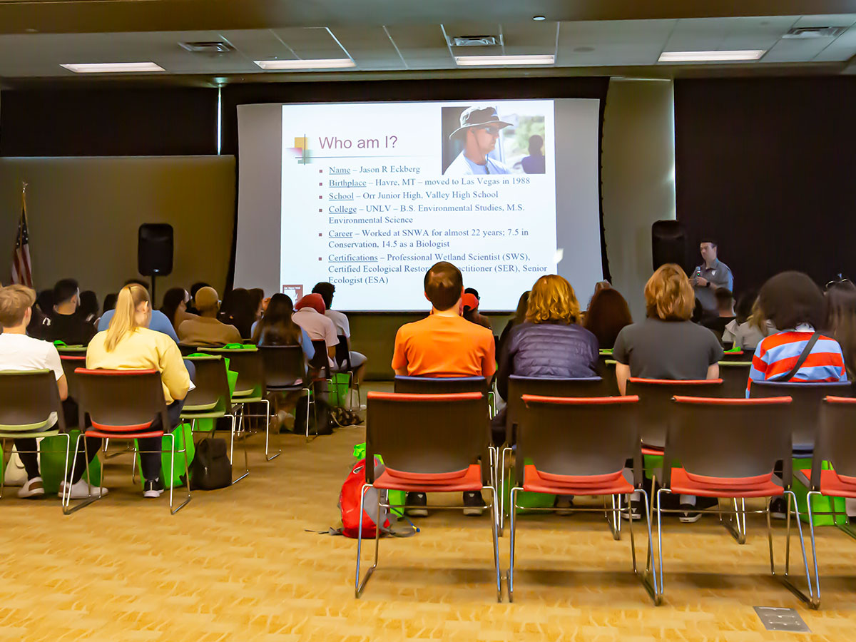 Students sit in an amphitheater watching a presentation by a biologist