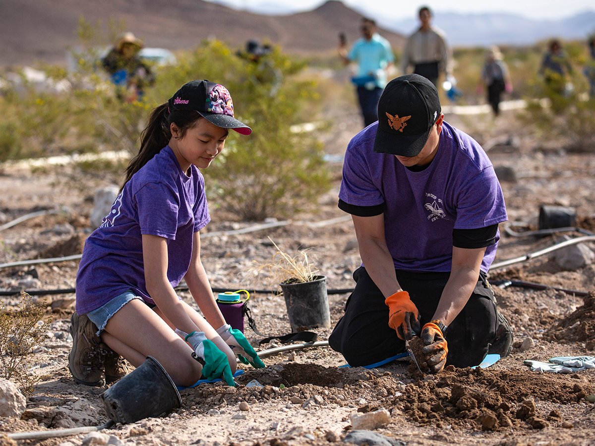 A pair of volunteers sit in the dirt at the Las Vegas Wash digging holes with shovels to plant flowers, grasses, and shrubs